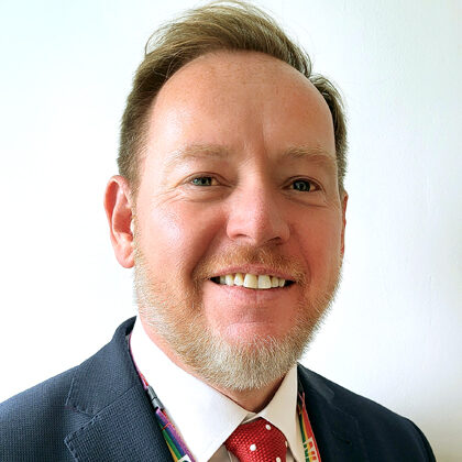 Mark Greatrex in suit and tie with rainbow NHS lanyard