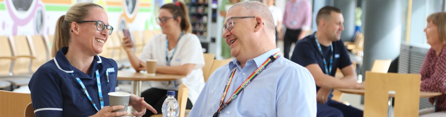 WCHC colleagues sat in St Catherine's Health Centre cafe, talking and smiling, wearing NHS lanyards