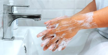 Hands under running water, washing with soap between fingers
