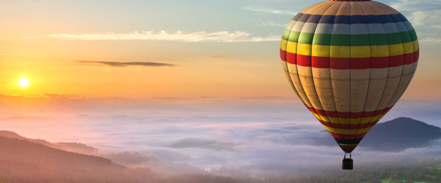 Hot air balloon flying over clouds, sunrise and mountains